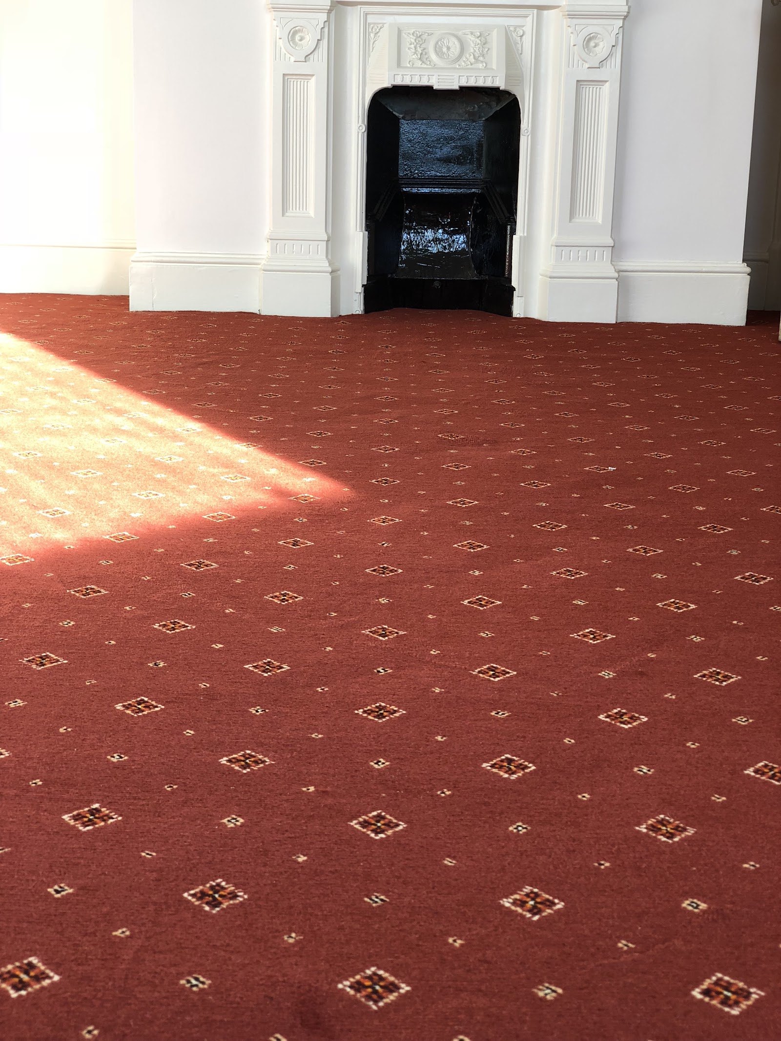 Red patterned carpet fitted in a room with a period fireplace