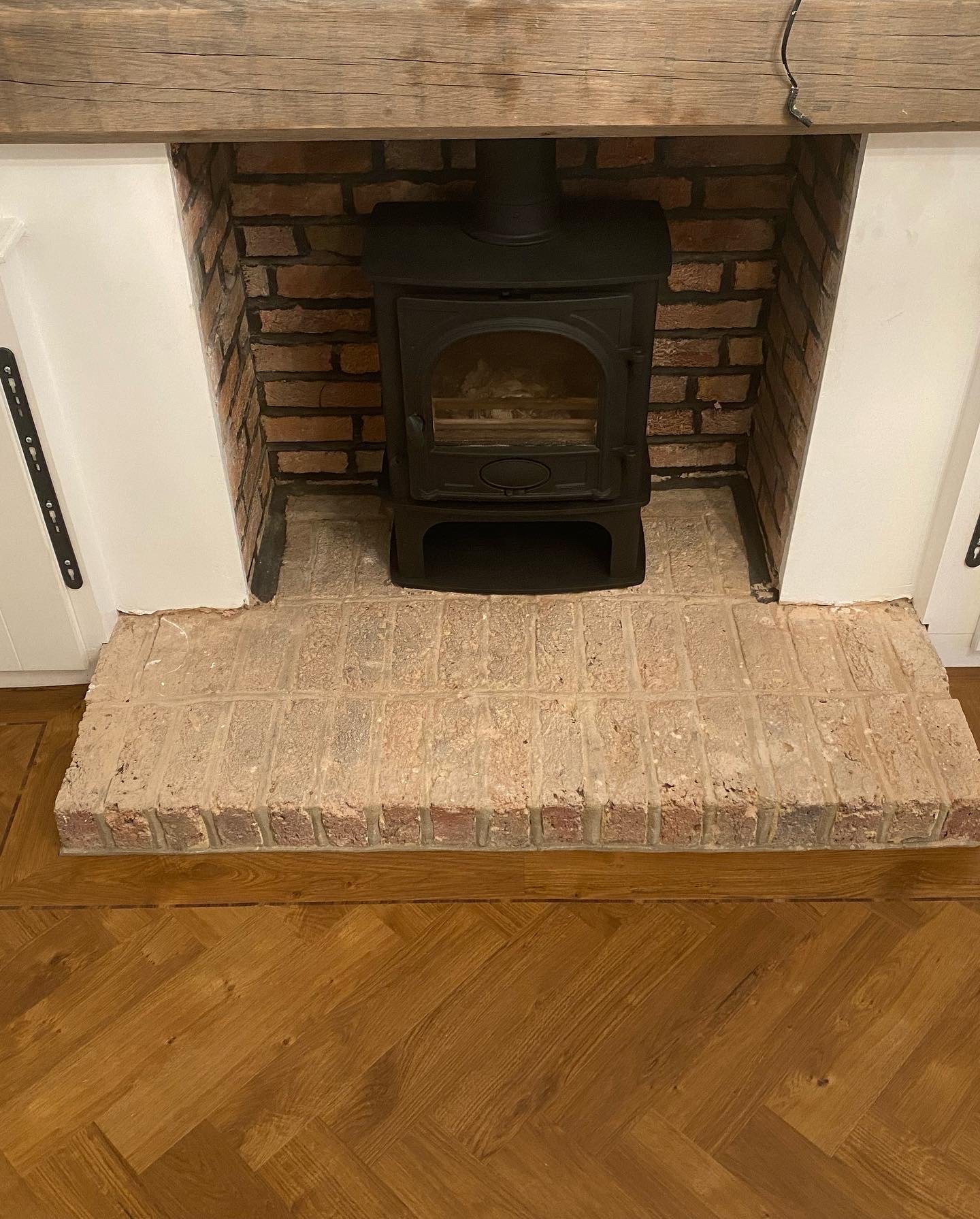 Oak herringbone floor meeting a raised brick hearth with a log burner