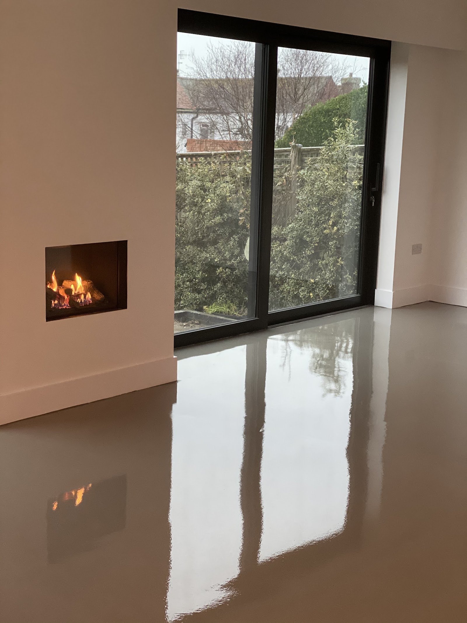 Glossy freshly poured liquid screed reflecting a fireplace and glass doors
