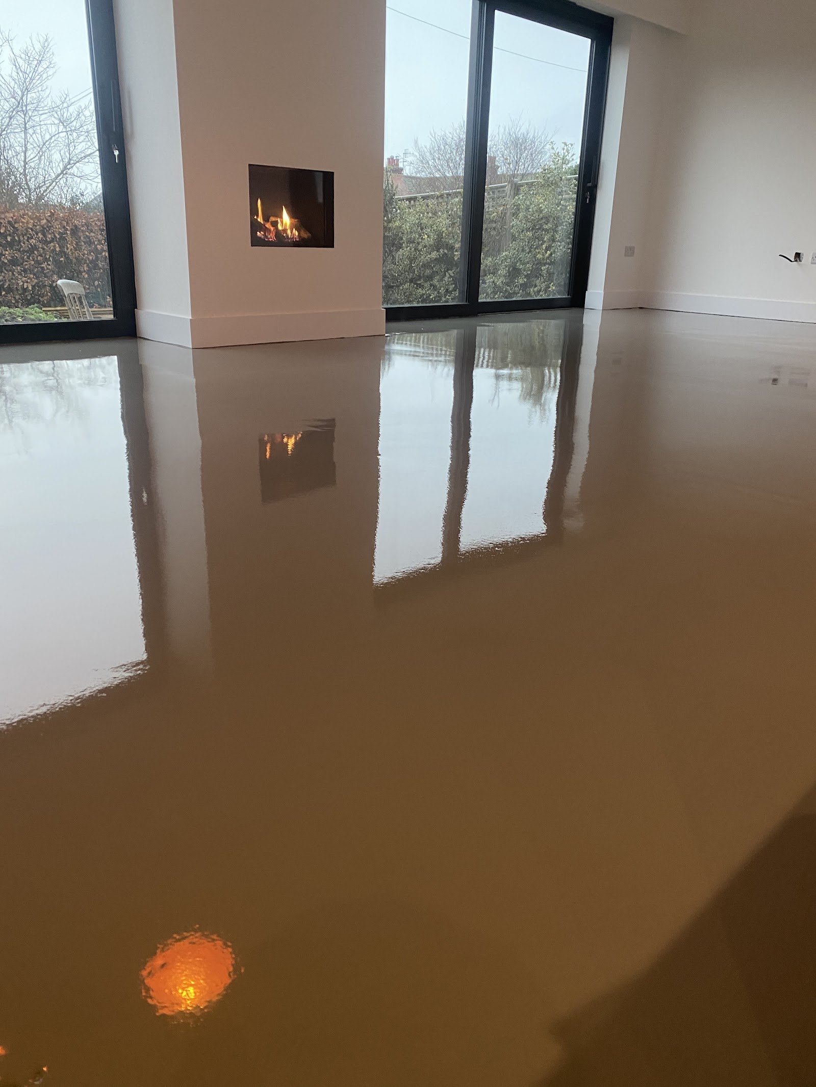 Freshly poured screed reflecting a wood burner and garden doors
