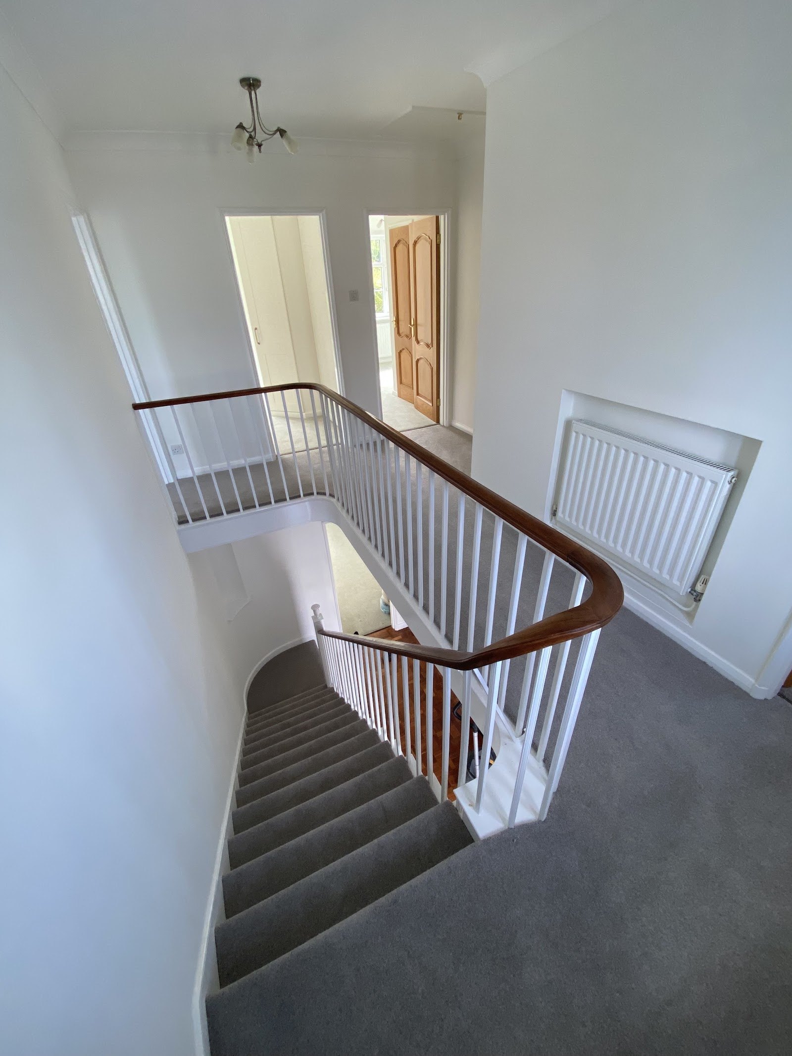 Bright landing with grey carpet looking down a white and mahogany staircase