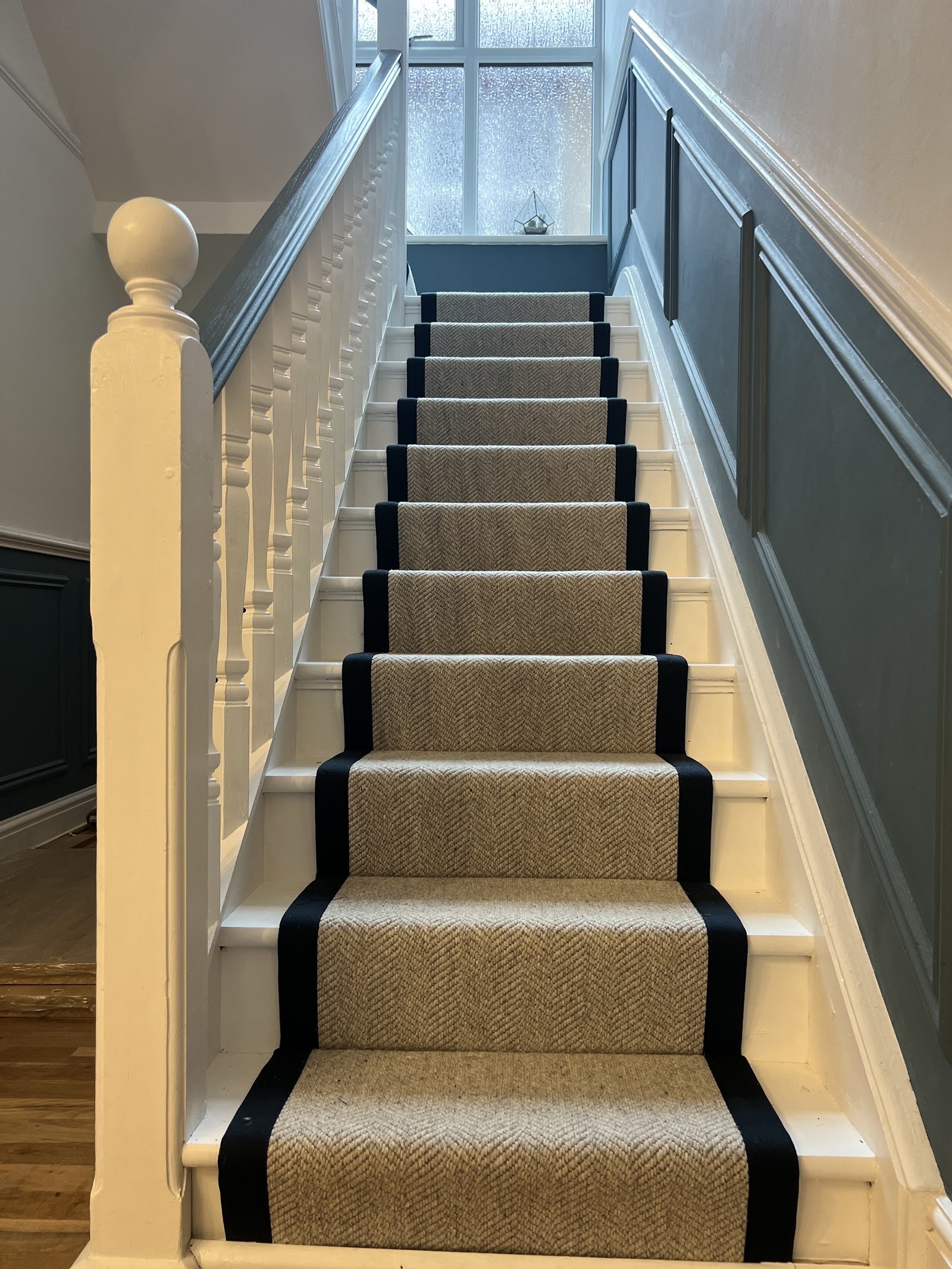 Natural stair runner with black border fitted up a white painted staircase