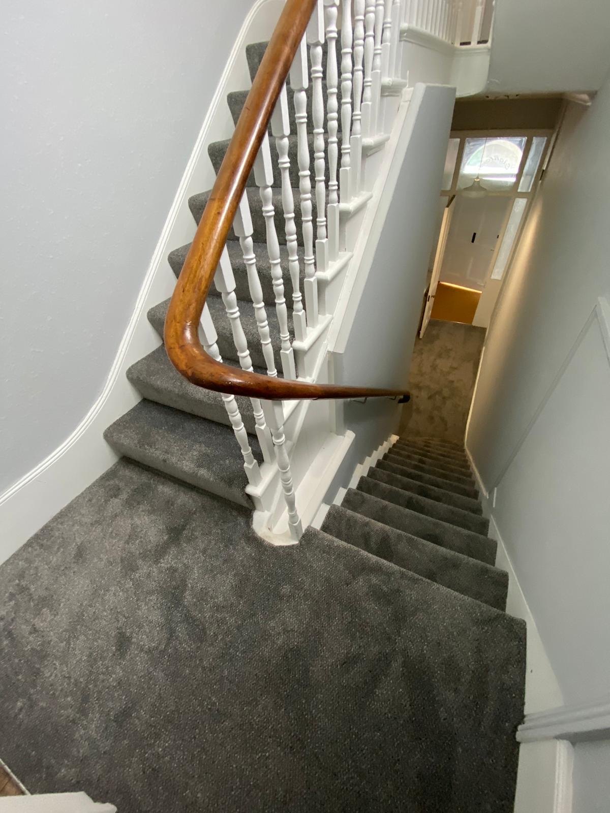 Grey carpet on a staircase with a mahogany handrail